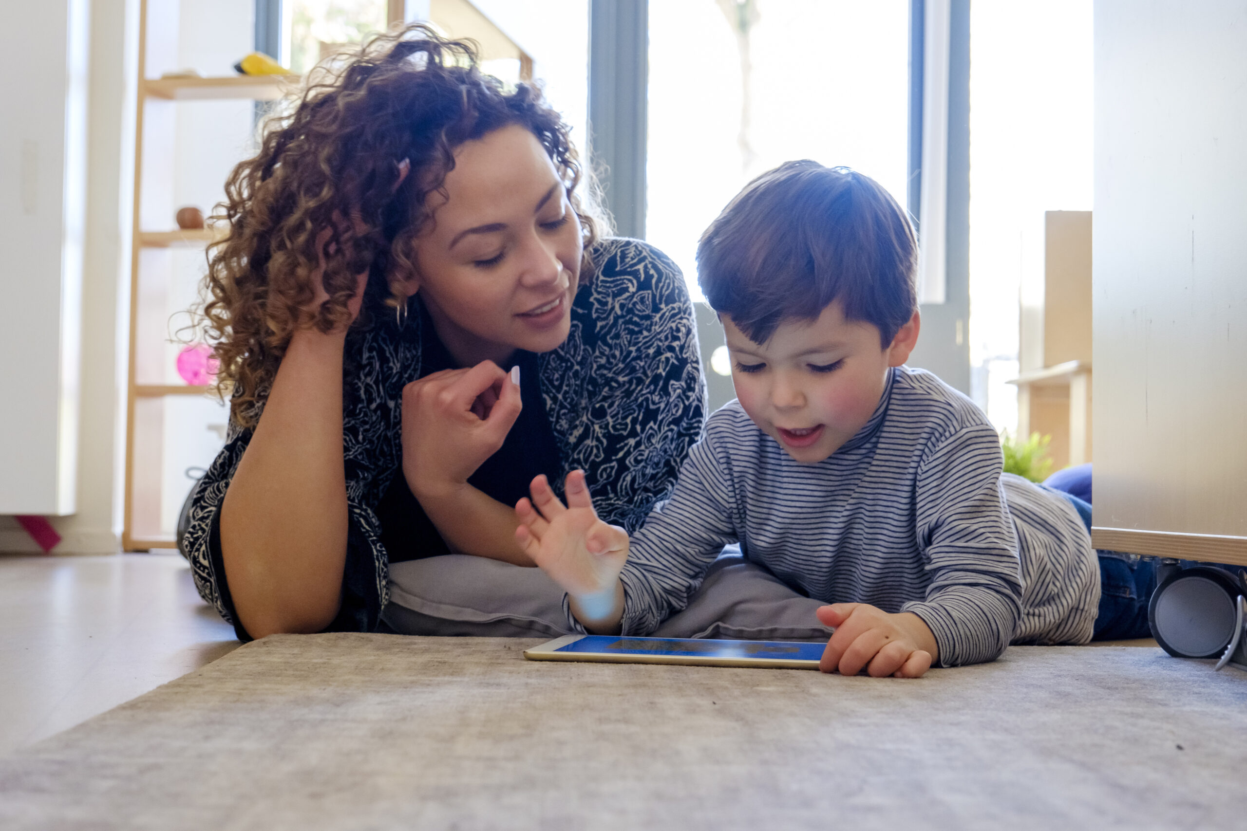 Moeder en zoon spelen liggend op de buik met de tablet, illustratie bij artikel gezond mediagebruik ukkies