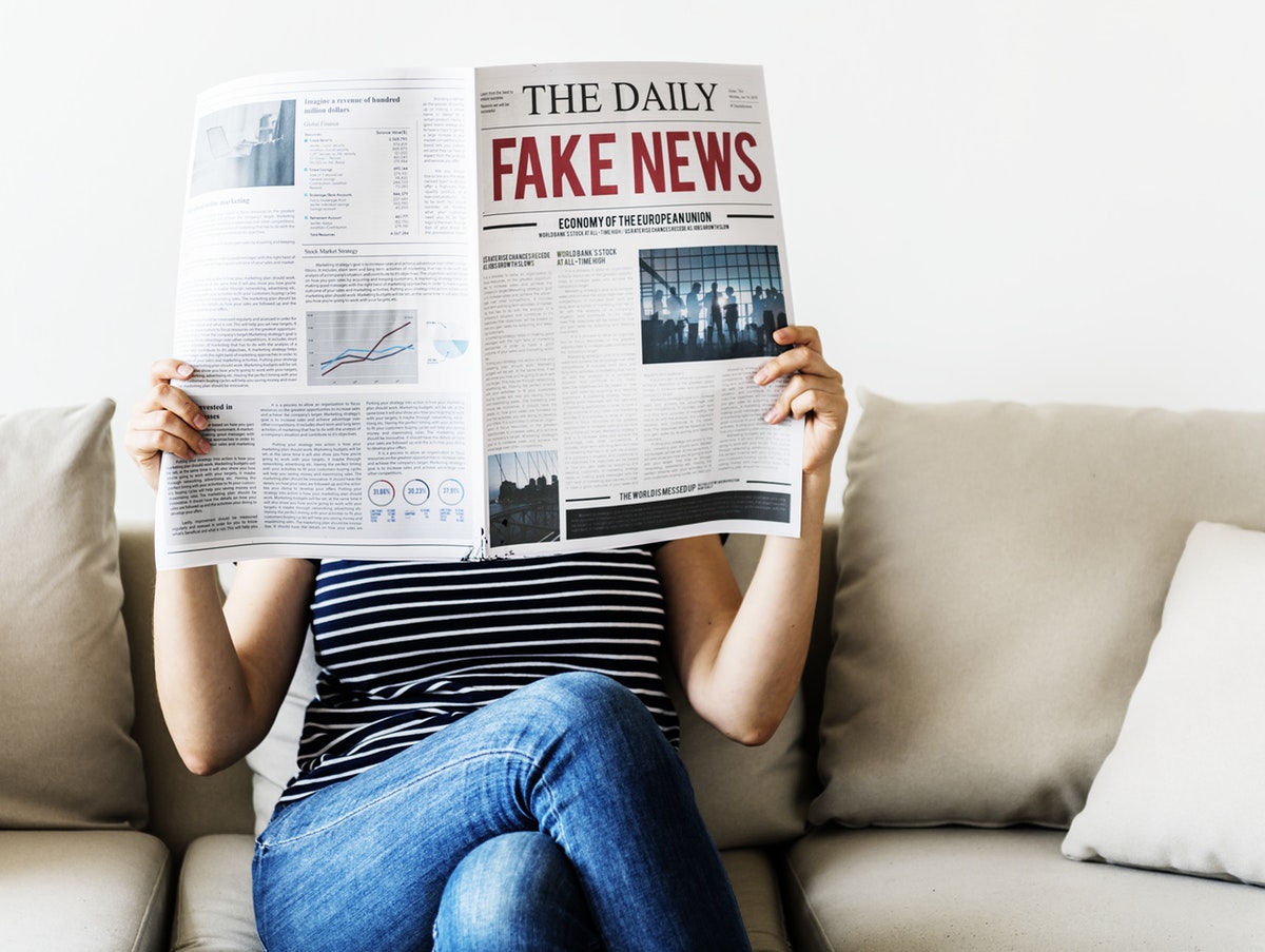Iemand op de bank, benen over elkaar gekruist. Leest een krant met grote rode letters met Fake News erop.