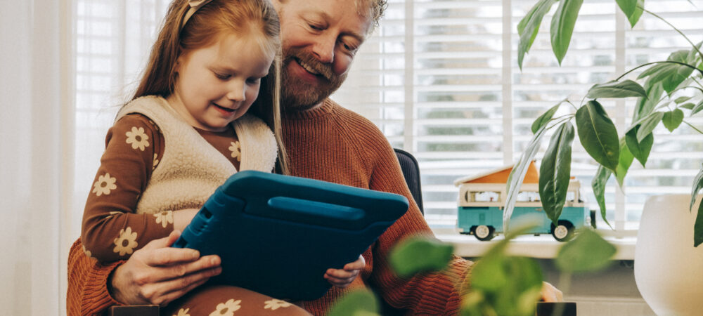 kind zit op schoot van ouder. ze zijn samen bezig met een tablet.