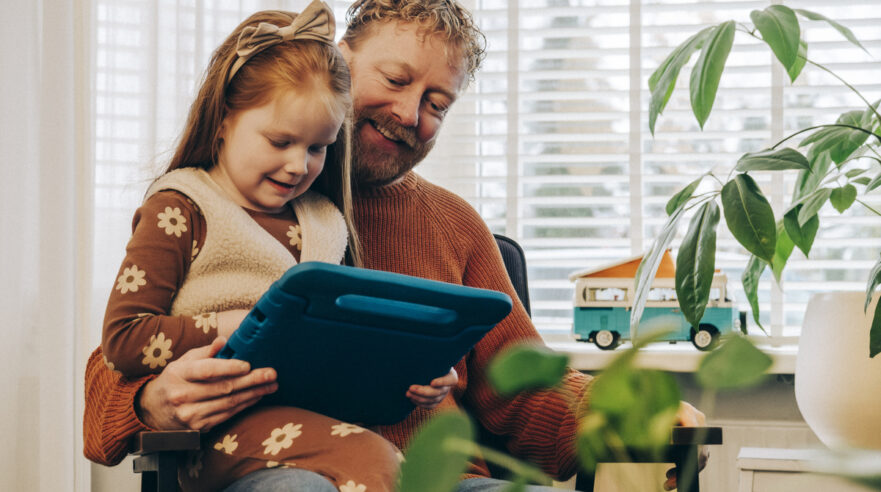 kind zit op schoot van ouder. ze zijn samen bezig met een tablet.