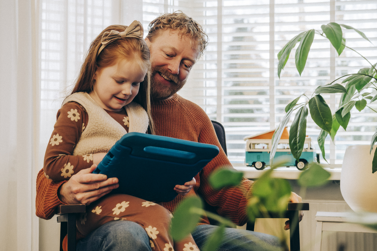 kind zit op schoot van ouder. ze zijn samen bezig met een tablet.