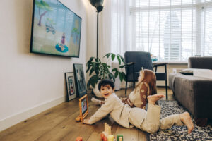 twee kinderen, de een kijkt vrolijk op van zijn tablet en de ander kijkt geconcentreerd naar de tv.