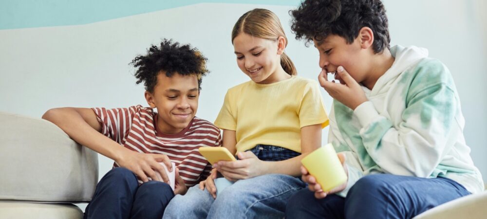 Drie kinderen van rond de 10 lachen naar een smartphone.