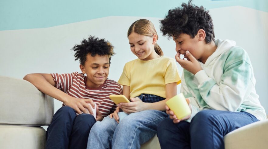 Drie kinderen van rond de 10 lachen naar een smartphone.