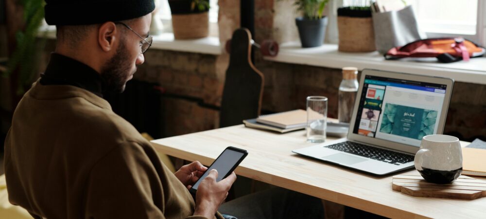 Een jongeman zit op z'n telefoon terwijl er een powerpoint afspeelt op zijn laptop.