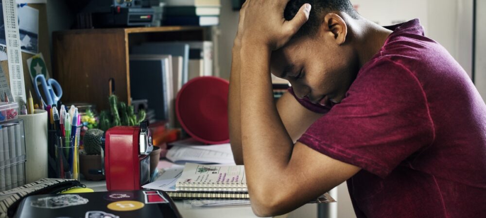 Jongen zit aan bureau met zijn handen op zijn hoofd