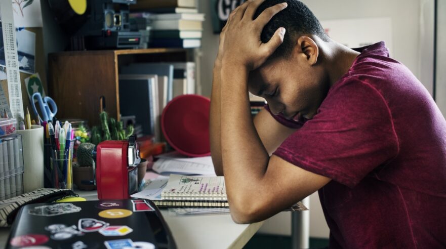 Jongen zit aan bureau met zijn handen op zijn hoofd