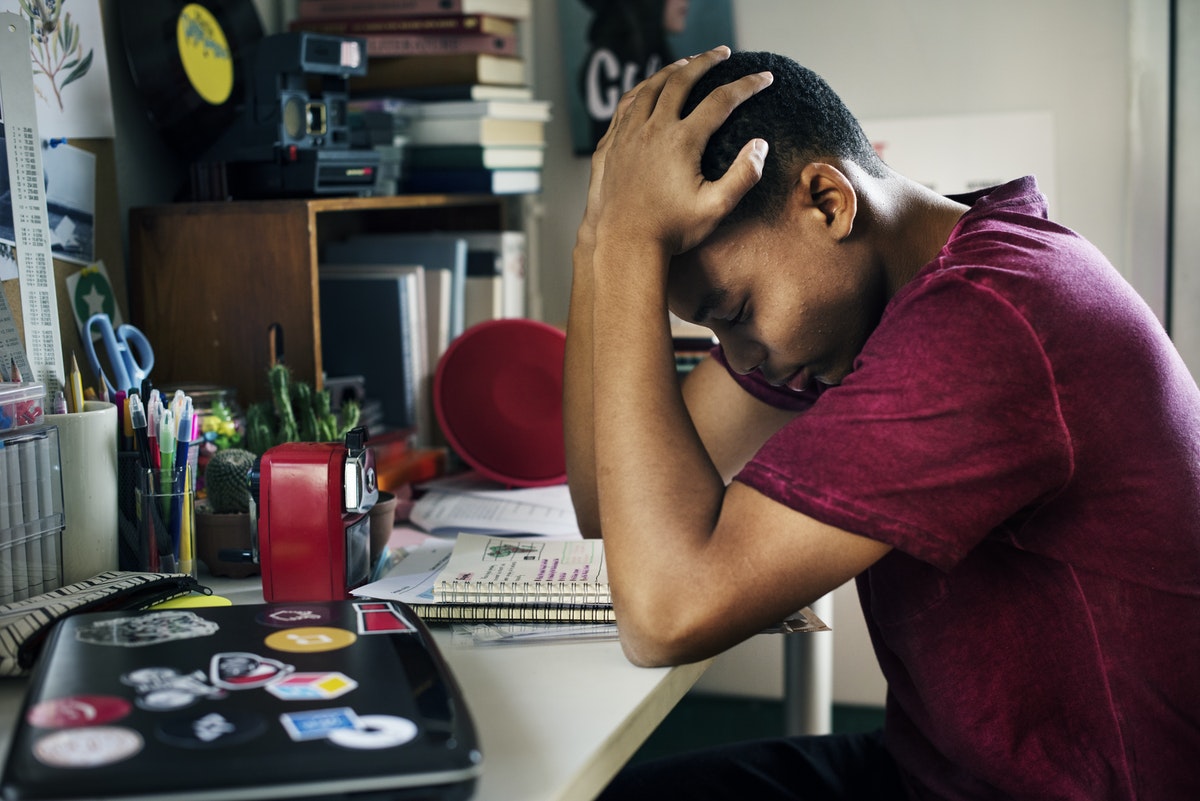 Jongen zit aan bureau met zijn handen op zijn hoofd